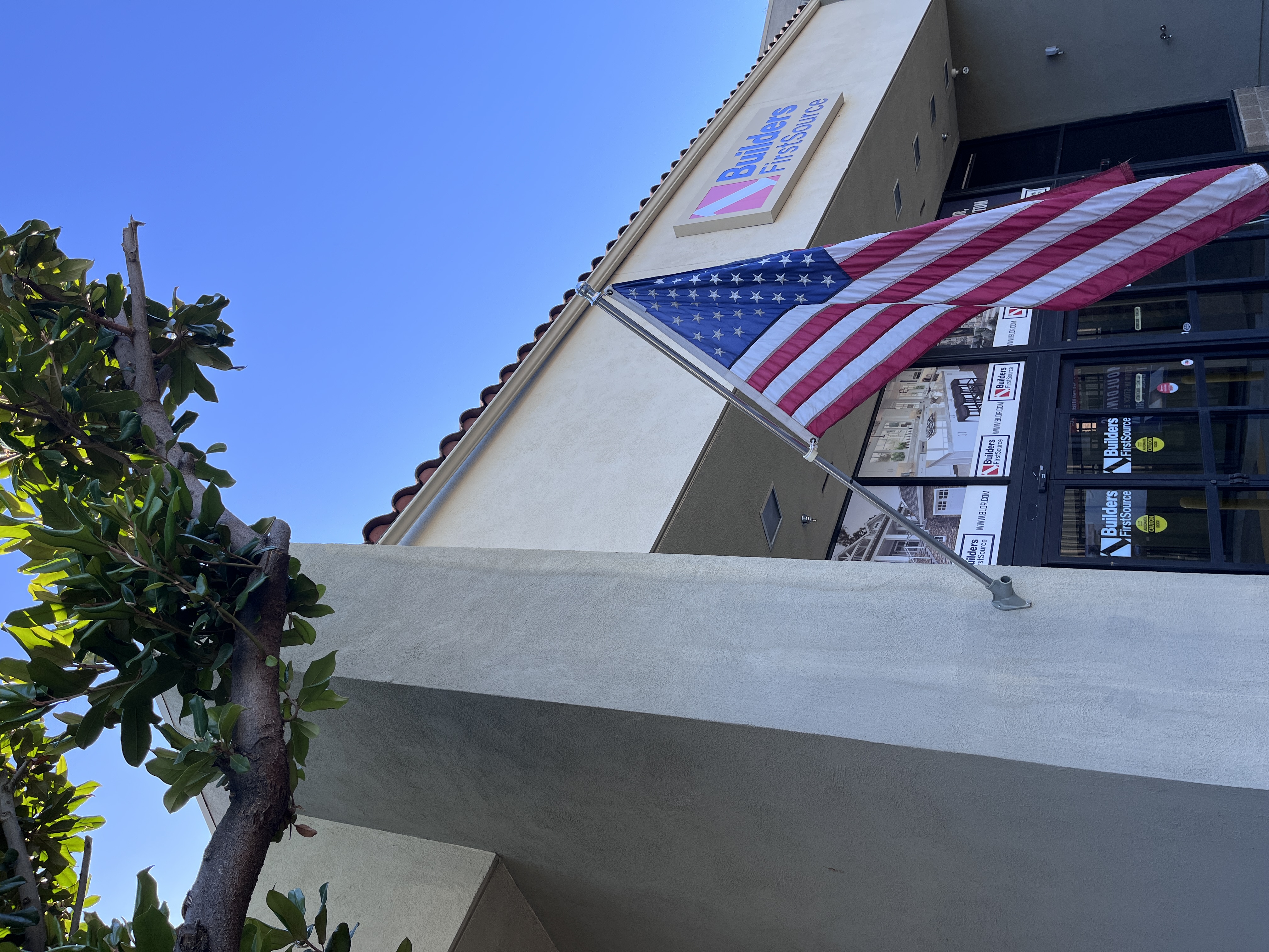 American flag mounted on the exterior of the Builders FirstSource Thousand Oaks, CA storefront beneath a tree branch.