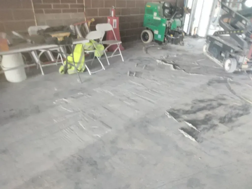 Worksite interior with damaged concrete floor, visible cracks and uneven surface, surrounded by tool 