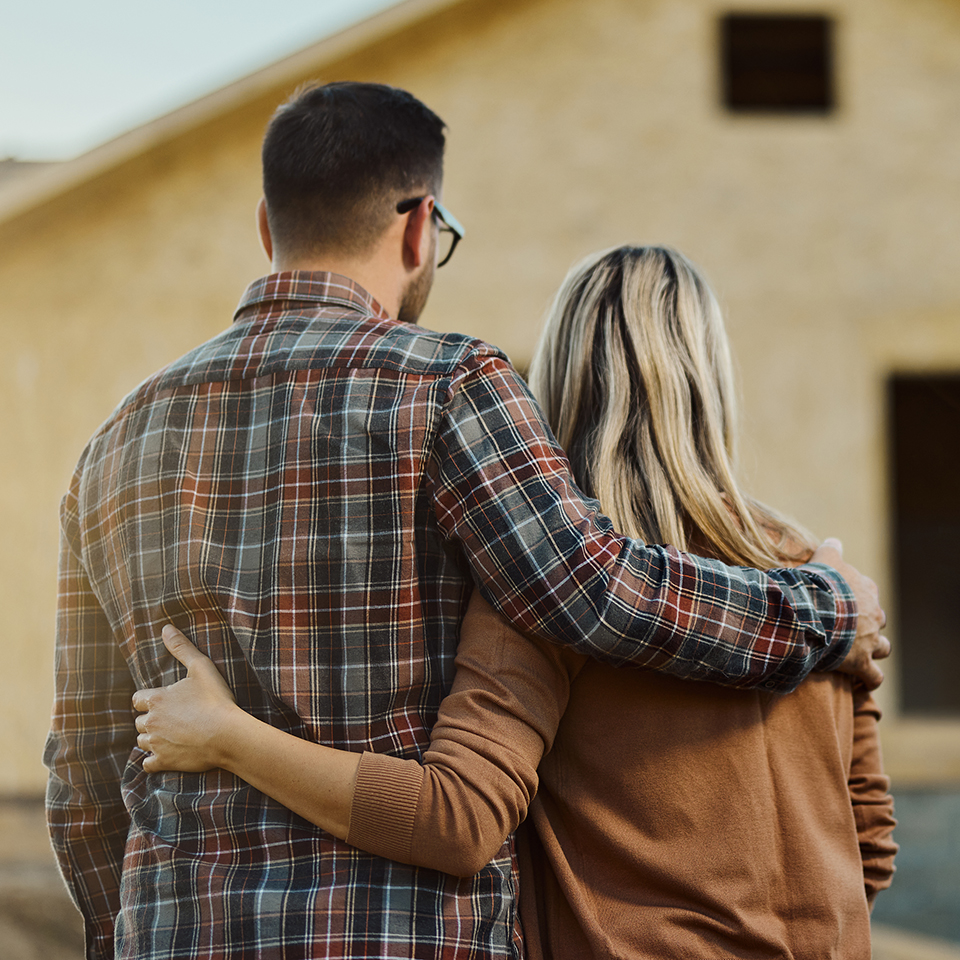 A man and woman with their arms around each other's waists looking at a home being built.