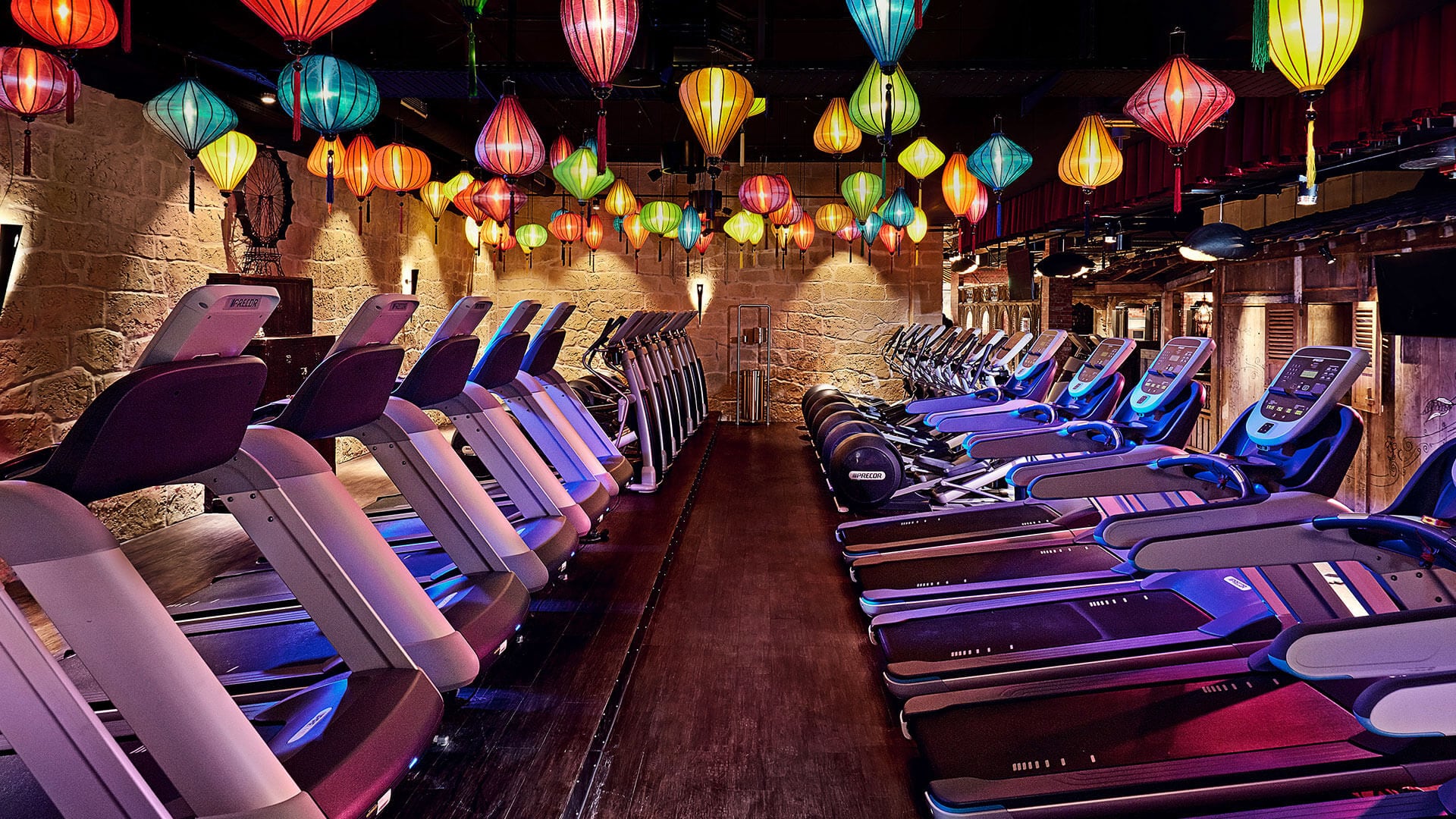 Rows of Treadmills in the interior of a McFit location underneath an arrangement of blue, green, orange and red paper lanterns.
