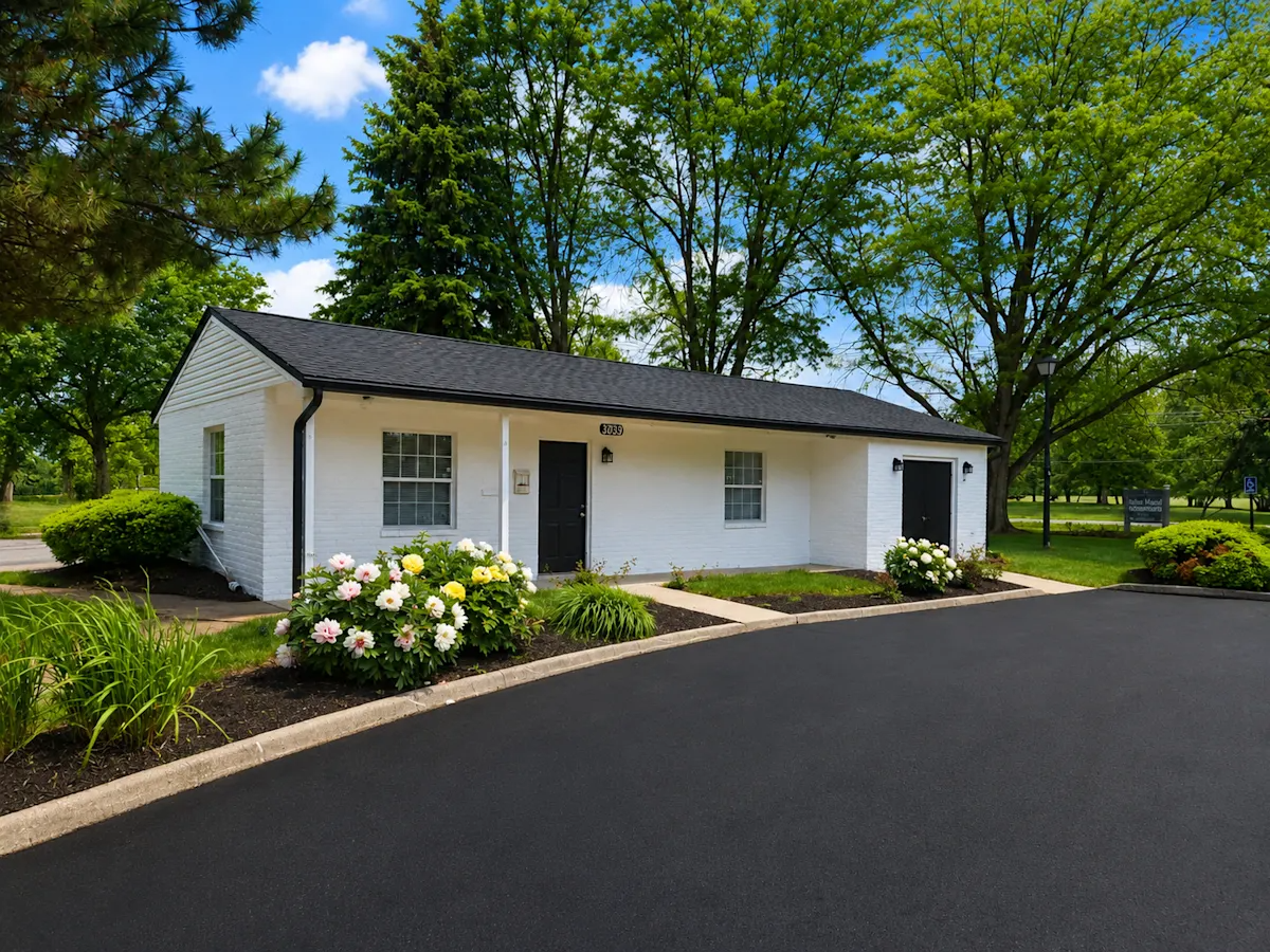 A white house with a black roof and a driveway in front.
