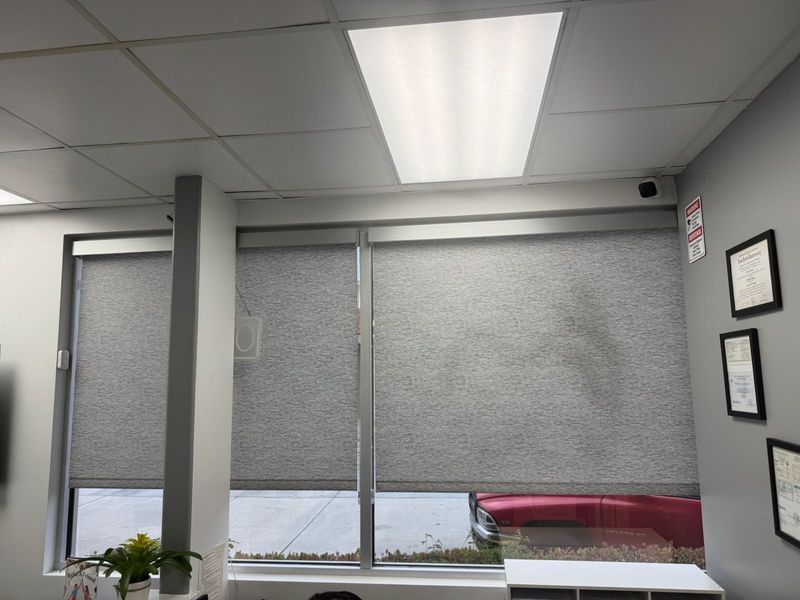 These custom gray roller shades offer a sleek, professional look for commercial office spaces. The textured fabric provides excellent glare reduction and privacy while maintaining a clean, minimalist interior design.