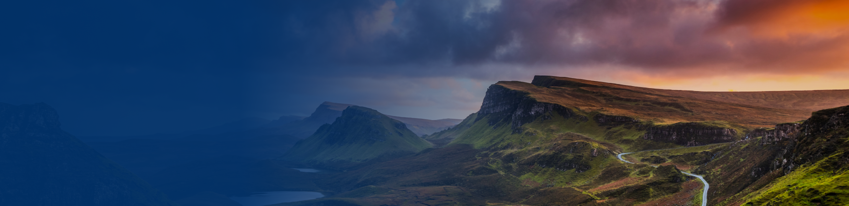A sweeping landscape of rolling hills under a dramatic cloudy-filled sky at dusk.
