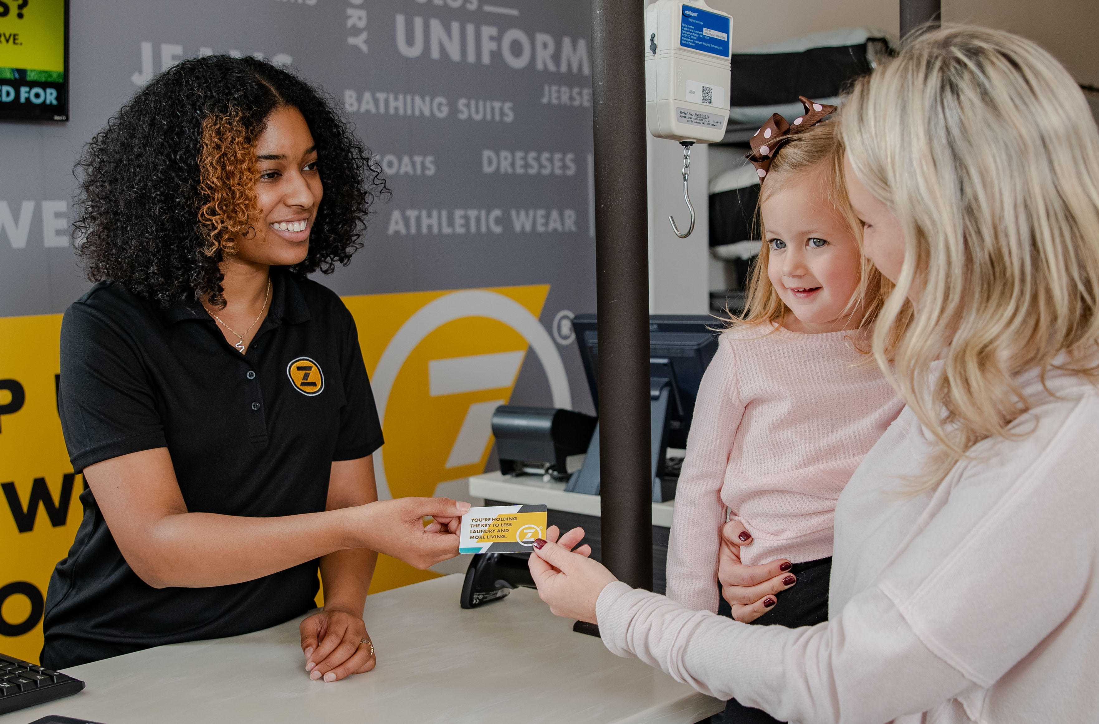A happy mom holding a child hands a friendly ZIPS Team Member a ZIPS Gift Card. ZIPS Cleaners is a mom's best friend, and so is a ZIPS Cleaners Gift Card, good on any of our services.