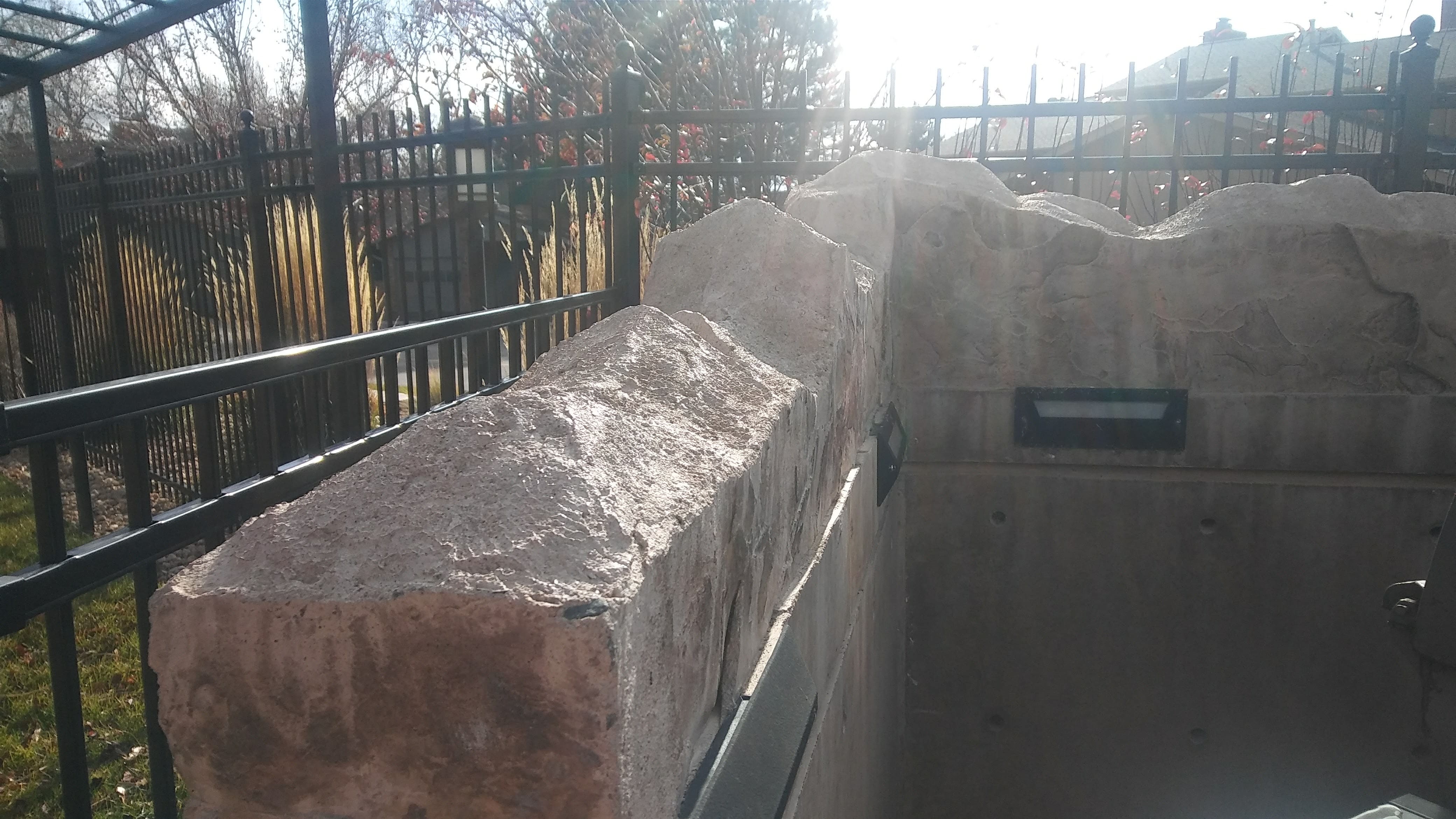 Custom concrete retaining wall with a textured stone-style finish, designed to provide structure while complementing the surrounding landscape and fencing.