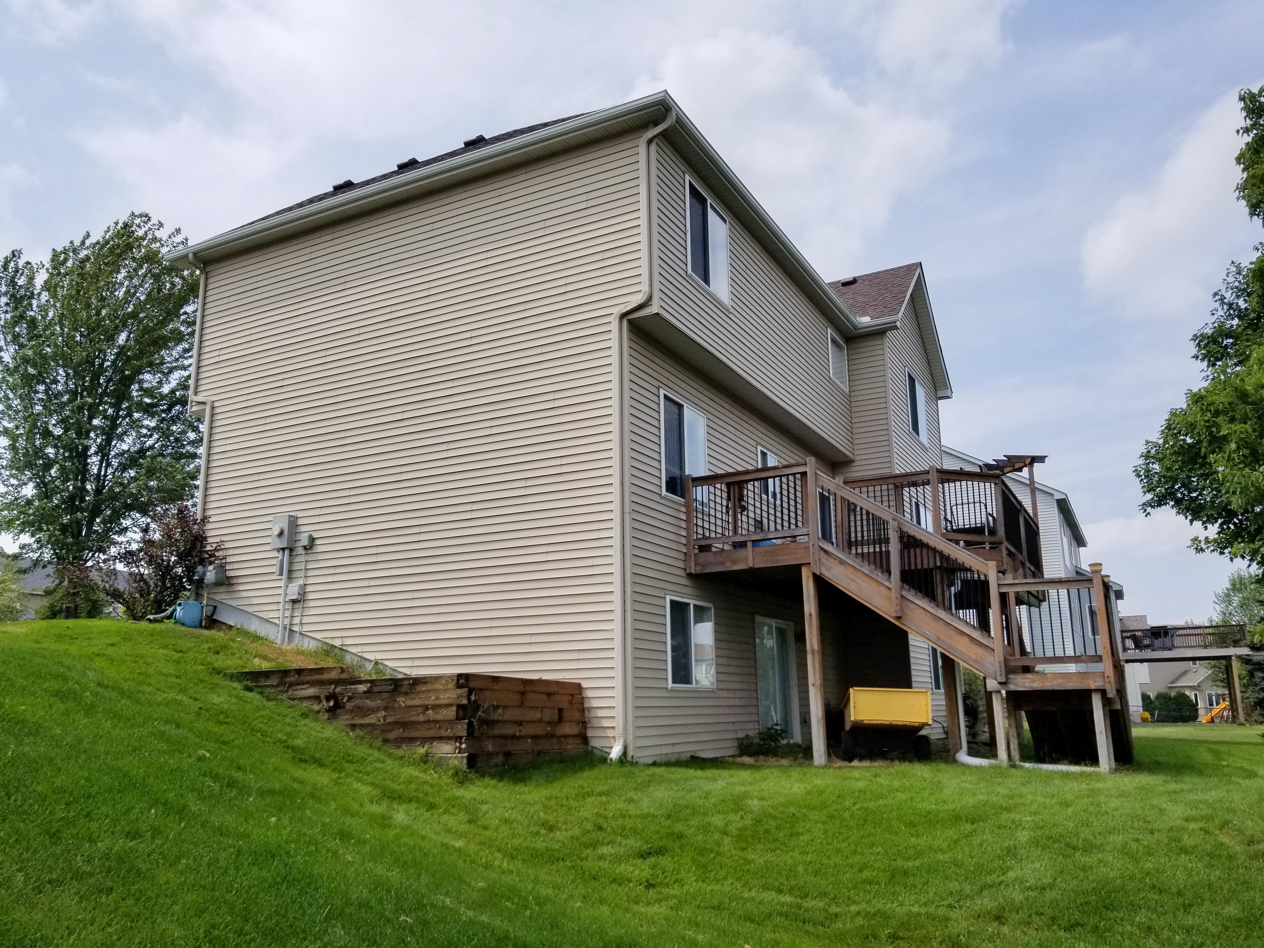 White seamless gutters and downspout system installed on a multi-story tan home with a wooden deck by Ultimate Gutter Solutions.