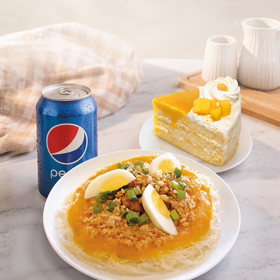 A plated meal featuring rice noodles, minced meat, green onions, and hard-boiled eggs, served alongside a blue Pepsi can and a slice of layered cake on a marble tabletop.