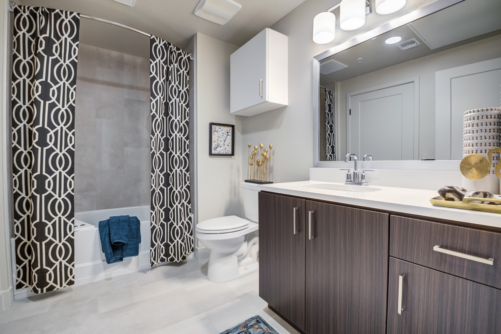 Tiled bathroom with quartz counters, framed mirror, and tiled shower.