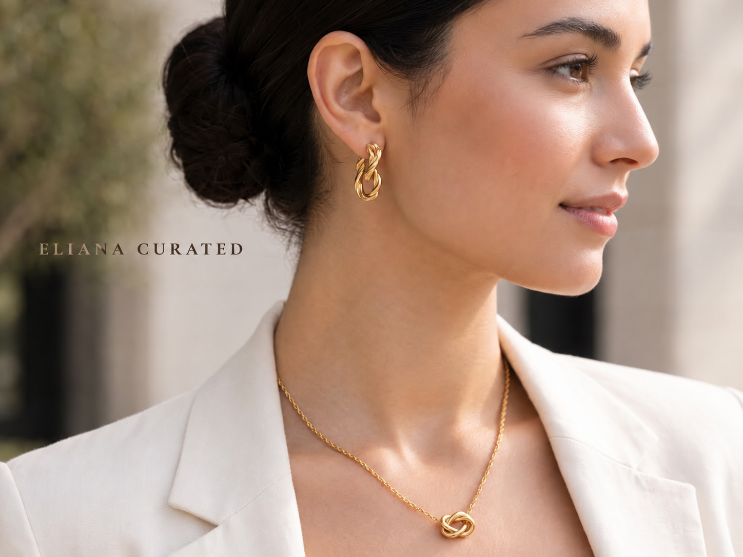 The model in a white blazer and matching top wears striking gold earrings and a delicate pendant nec 