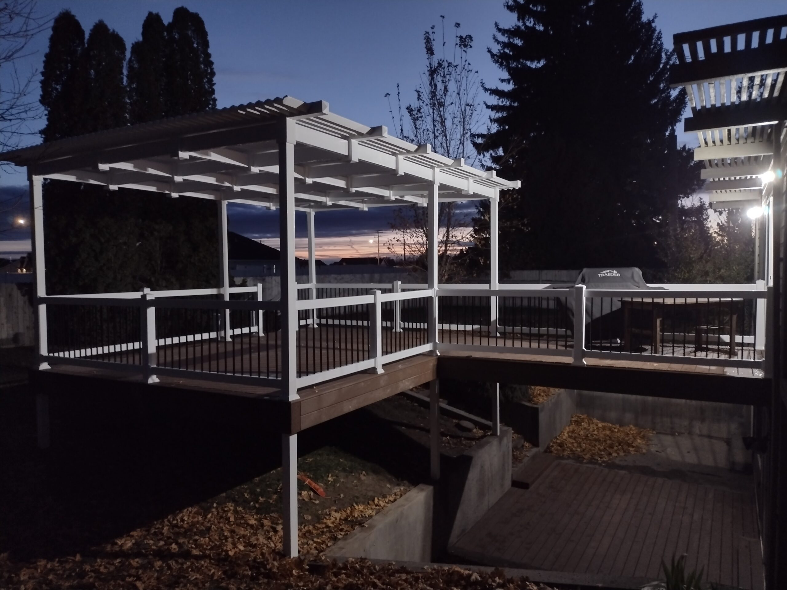 Extend your outdoor living hours with a stunning custom pergola from DeckPro LLC. This beautiful white pergola, pictured here at dusk, provides shade and structure to the raised composite deck, creating a perfect, defined space for evening relaxation and entertainment.