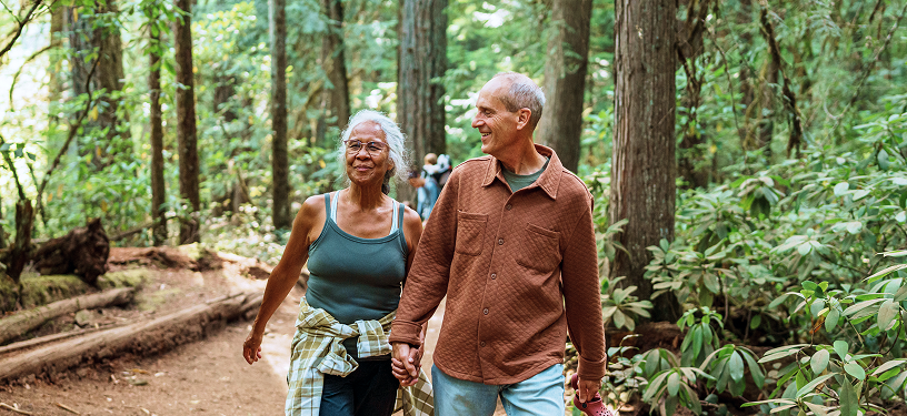 An elderly couple walking in the woods.
