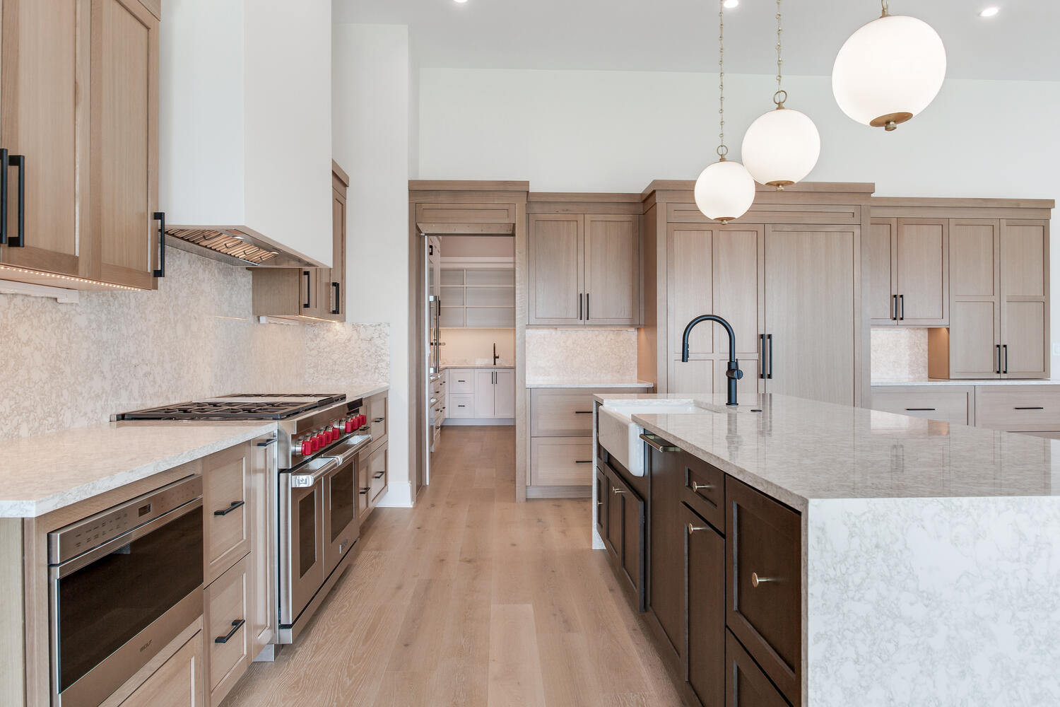 Custom kitchen with warm wood cabinetry, a spacious center island, stone countertops, stainless steel appliances, and bright contemporary lighting.