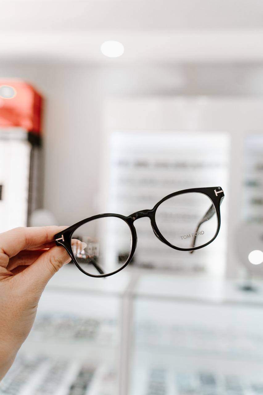 Hand holding black Tom Ford designer eyeglass frames with signature T-shaped details at TK Optometry 