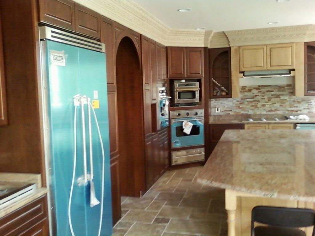 A modern kitchen featuring wooden cabinetry, granite countertops, and built-in stainless steel appliances. A large island provides workspace, while decorative backsplash tiles and crown molding enhance the elegant, functional design.