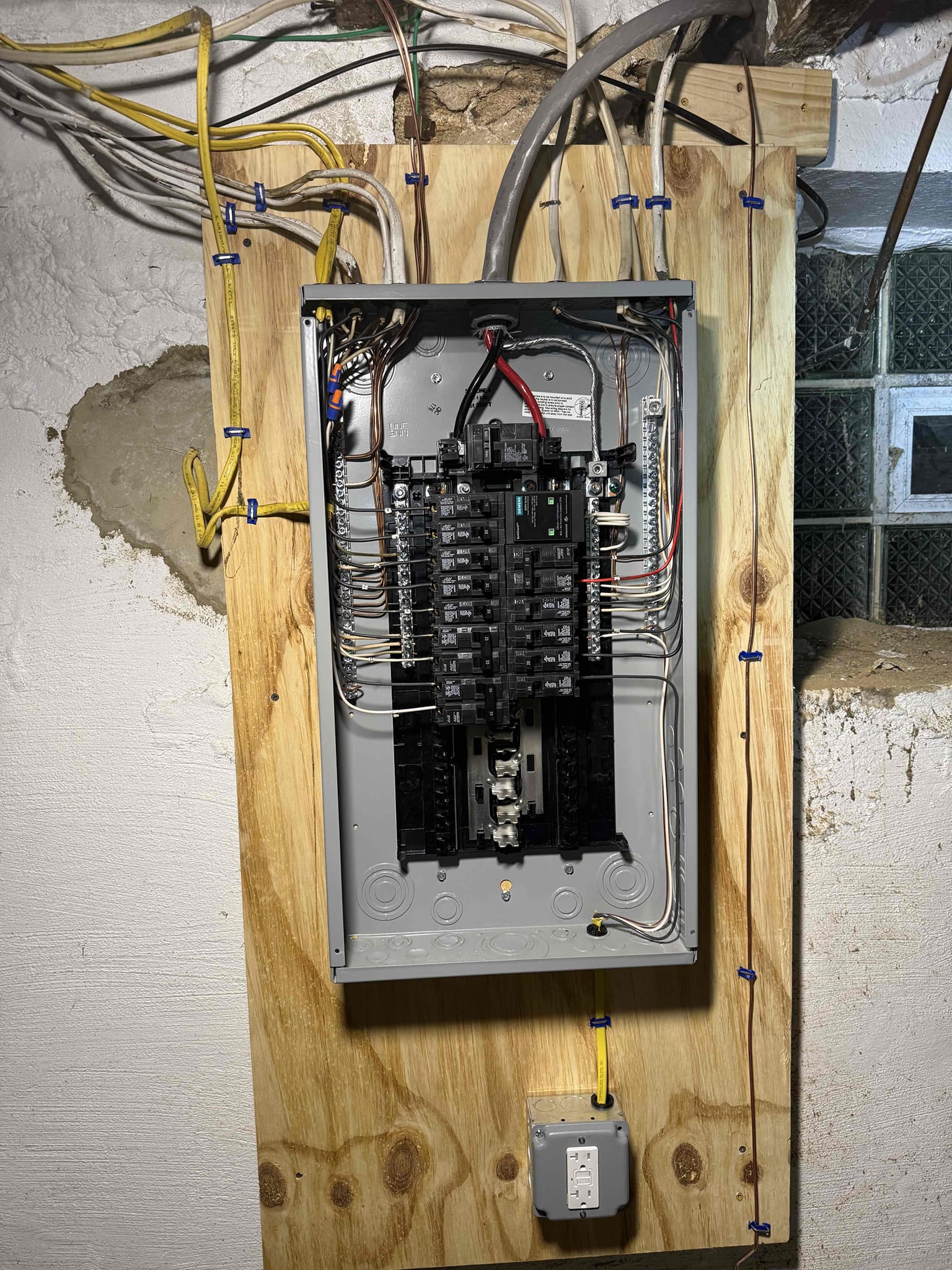 Thomas Edison Electric upgraded this breaker panel in a Philadelphia, PA basement near Cottman Ave. The panel is mounted on a treated plywood backer with neatly stapled Romex runs, and a GFCI outlet is installed directly below for convenient access.