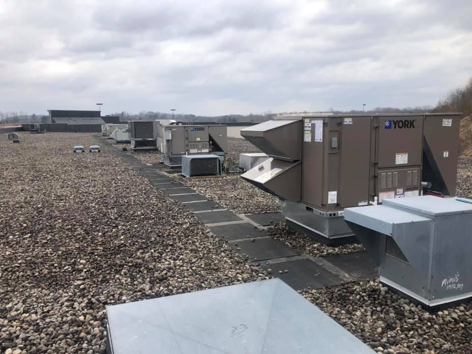 Multiple rooftop HVAC units installed across large commercial building, aligned along gravel surface with access paths, showcasing extensive heating and cooling system setup designed for large-scale climate control and maintenance accessibility.