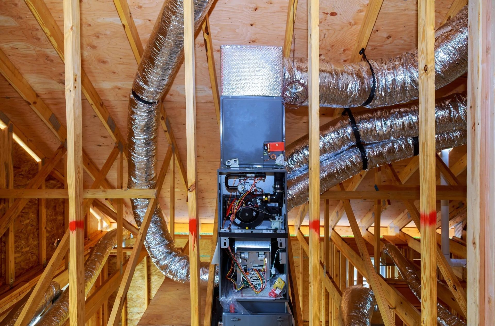 HVAC system installed in unfinished attic space with exposed wooden framing, insulated ductwork, and furnace unit, showcasing residential ventilation setup, airflow distribution, and mechanical components during construction or renovation process.
