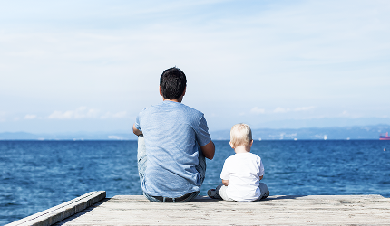 Father and toddler sitting by a lake and looking out at the view.
