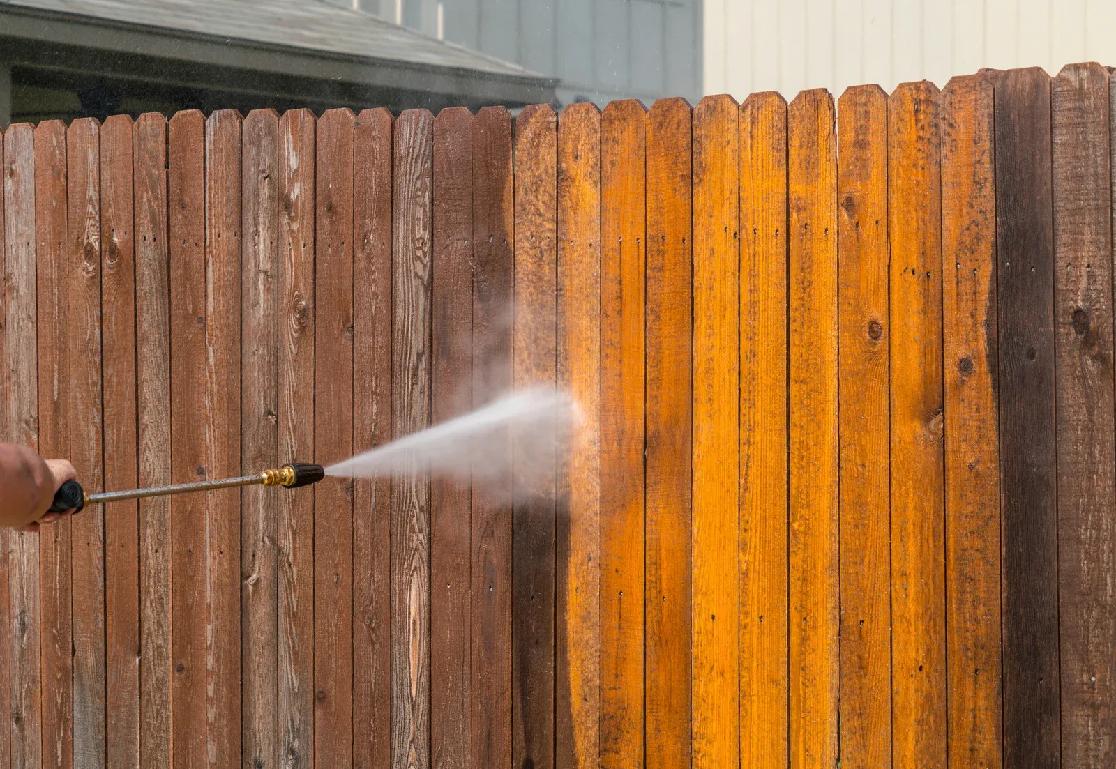 Worker using a pressure washer to clean a wooden fence, removing dirt and grime to reveal the original wood color. High-pressure water spray restores the fence&rsquo;s appearance, enhancing durability, cleanliness, and overall curb appeal of the outdoor space.
