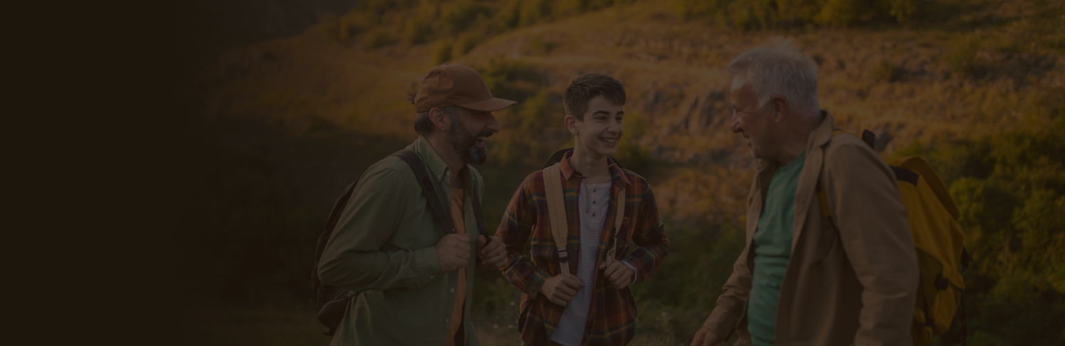 A grandfather, son, and grandson laughing together during a hike.