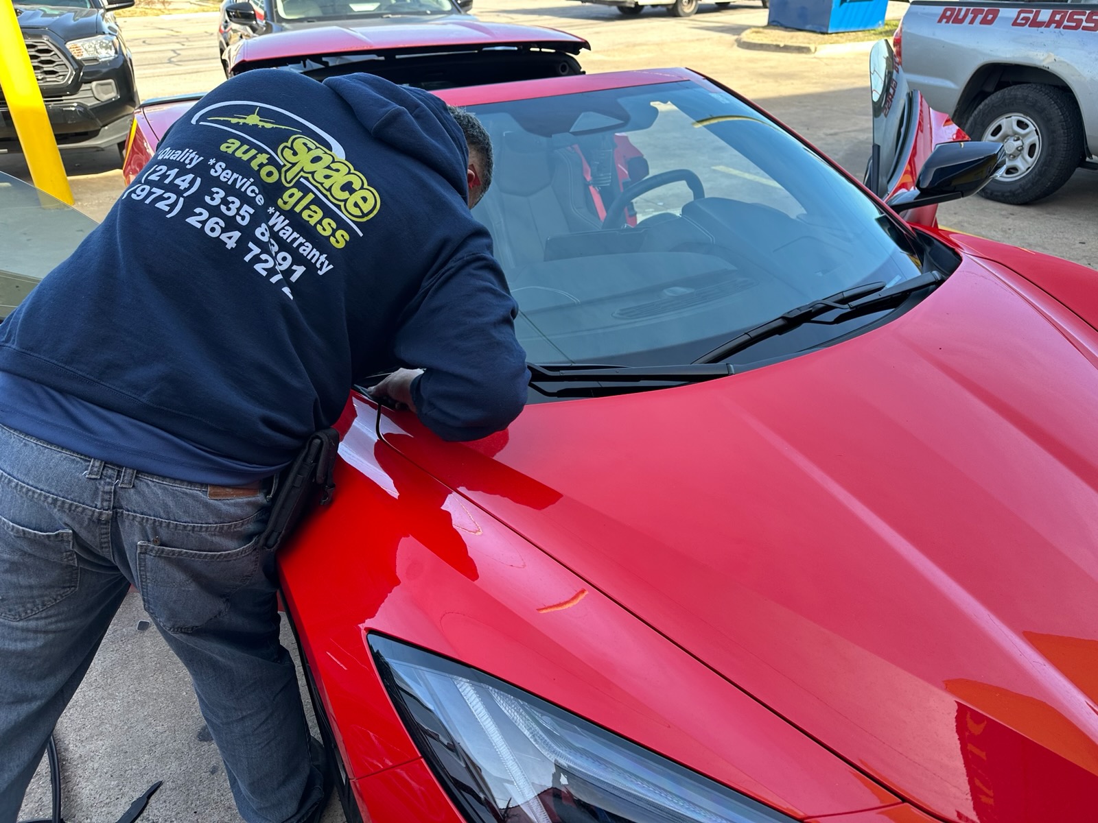 A Space Auto Glass technician works along the edge of a newly installed windshield on a red sports car. The image shows the hands-on installation process used to fit and secure replacement auto glass.