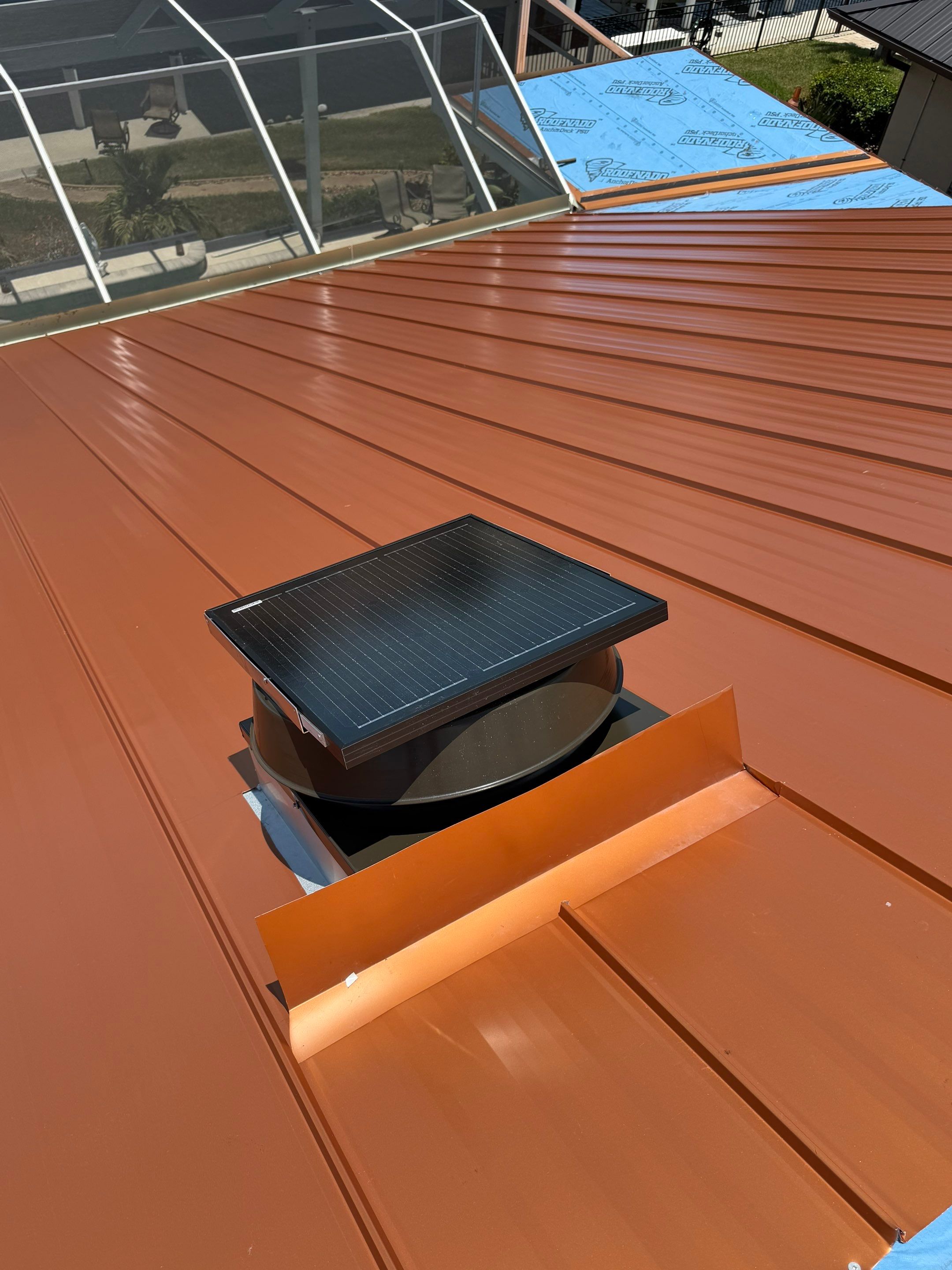 Roofer installing metal roofing panels over blue underlayment on a waterfront residential property. 