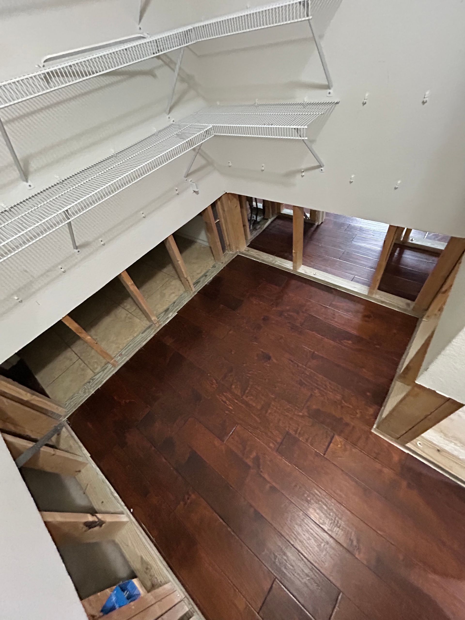 An interior closet or storage area shows sections of lower drywall removed, exposing wooden wall fra 