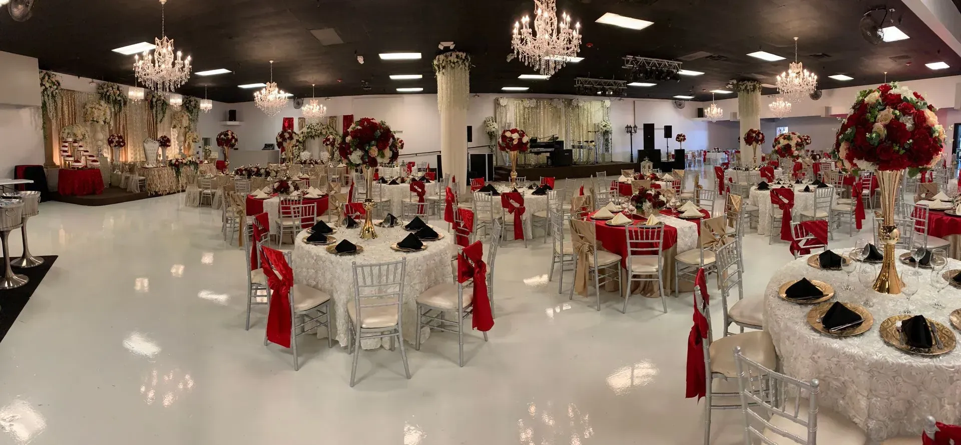 Spacious banquet hall featuring red and white wedding décor, crystal chandeliers, floral centerpiece 