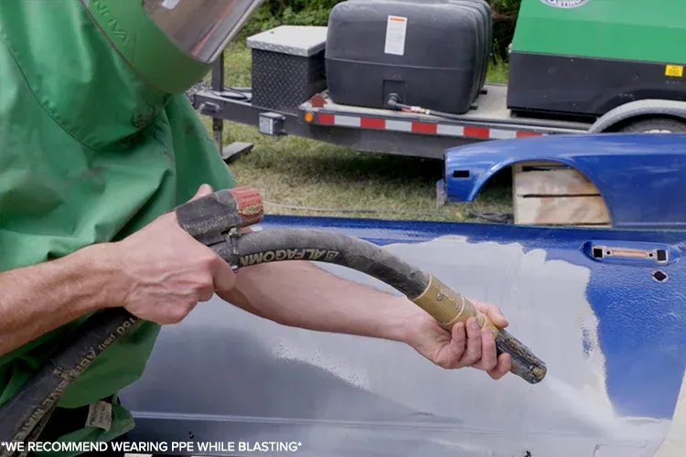 Close-up of technician performing abrasive blasting on metal car panel, removing paint layers and corrosion, ensuring smooth surface preparation for automotive refinishing, restoration, and long-lasting coating applications.