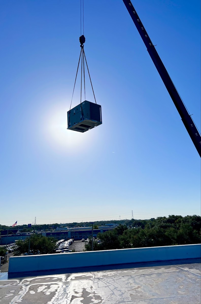Rooftop HVAC unit being crane-lifted into place for a commercial heating and cooling installation.