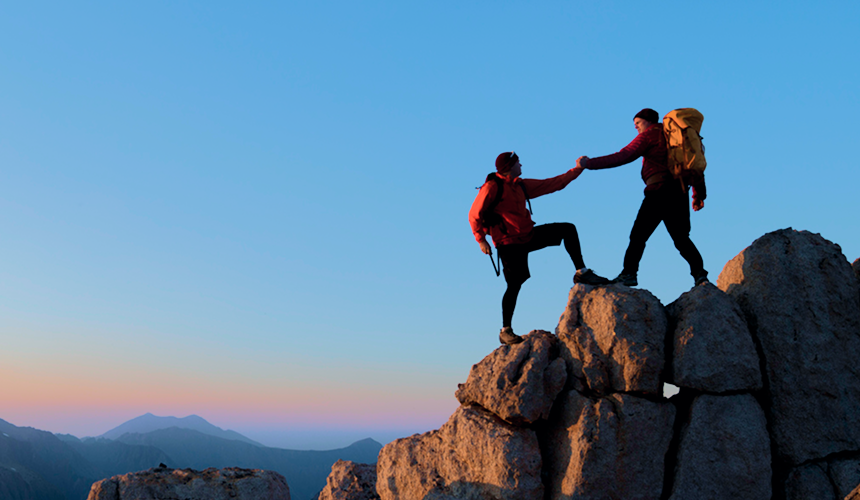 Two friends helping each other climb the peak of a mountain.