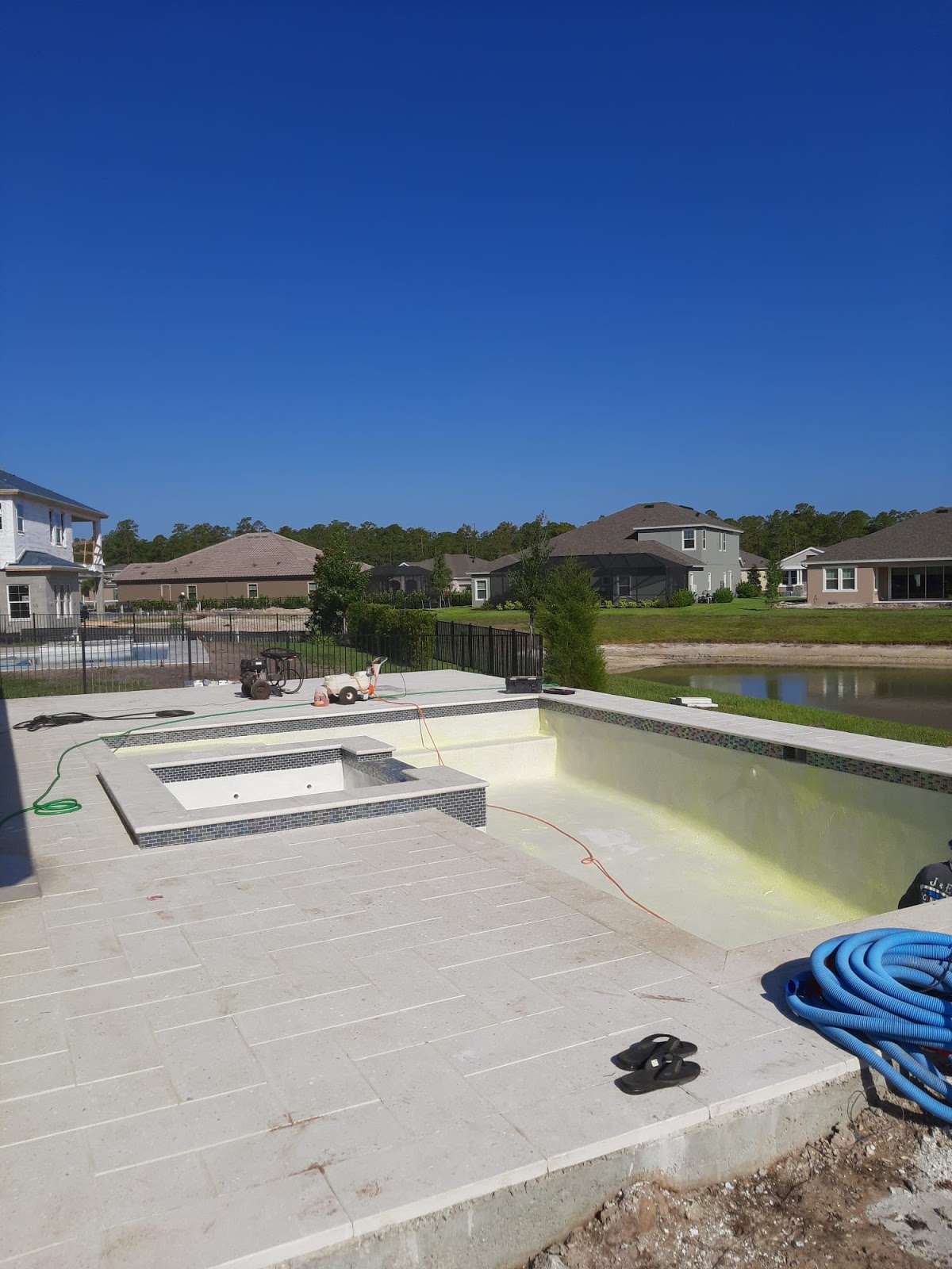 Residential swimming pool renovation in progress with an attached spa, light stone decking, and surrounding construction materials.