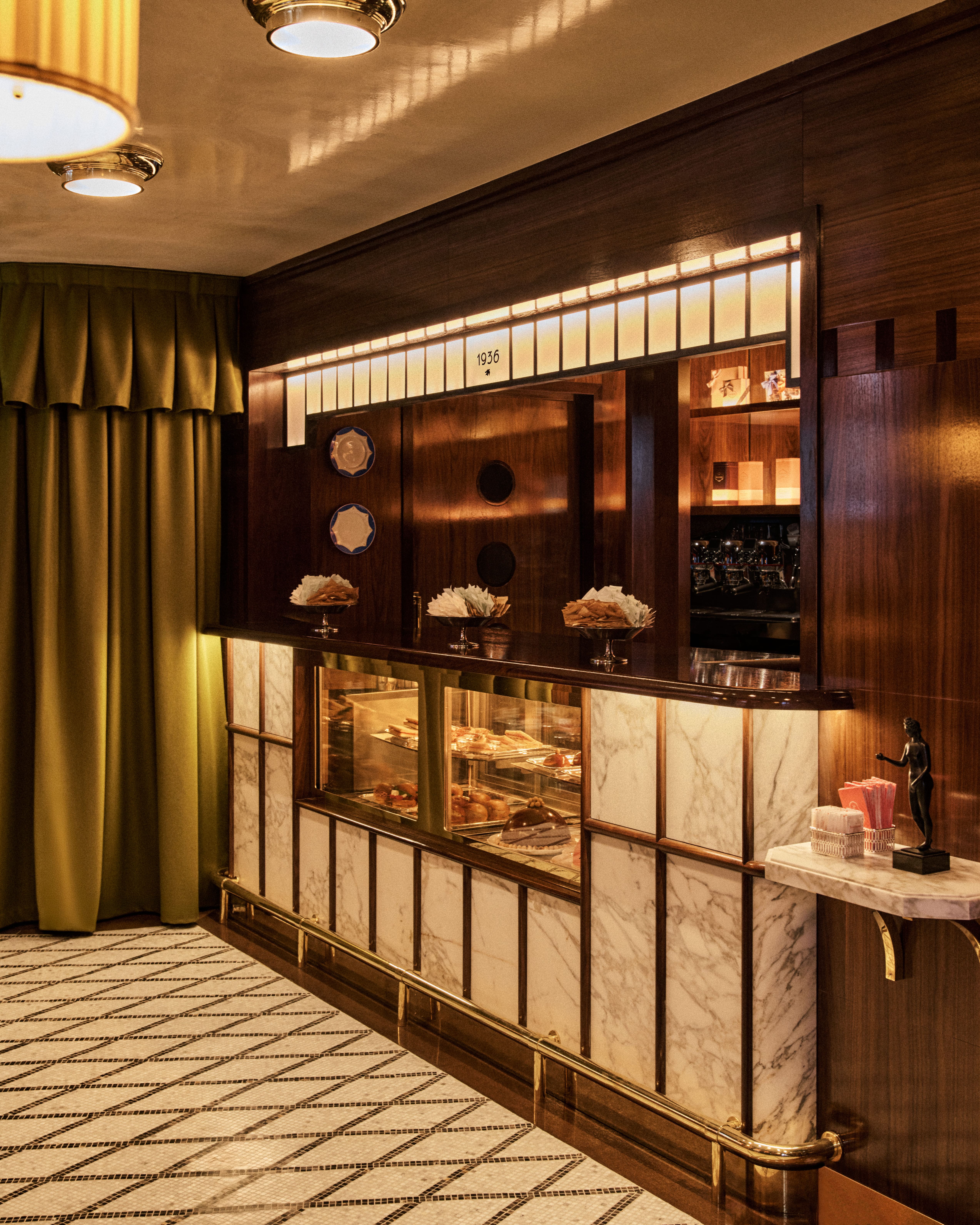 Art Deco pastry counter with marble panels, glass display, and warm wood detailing.