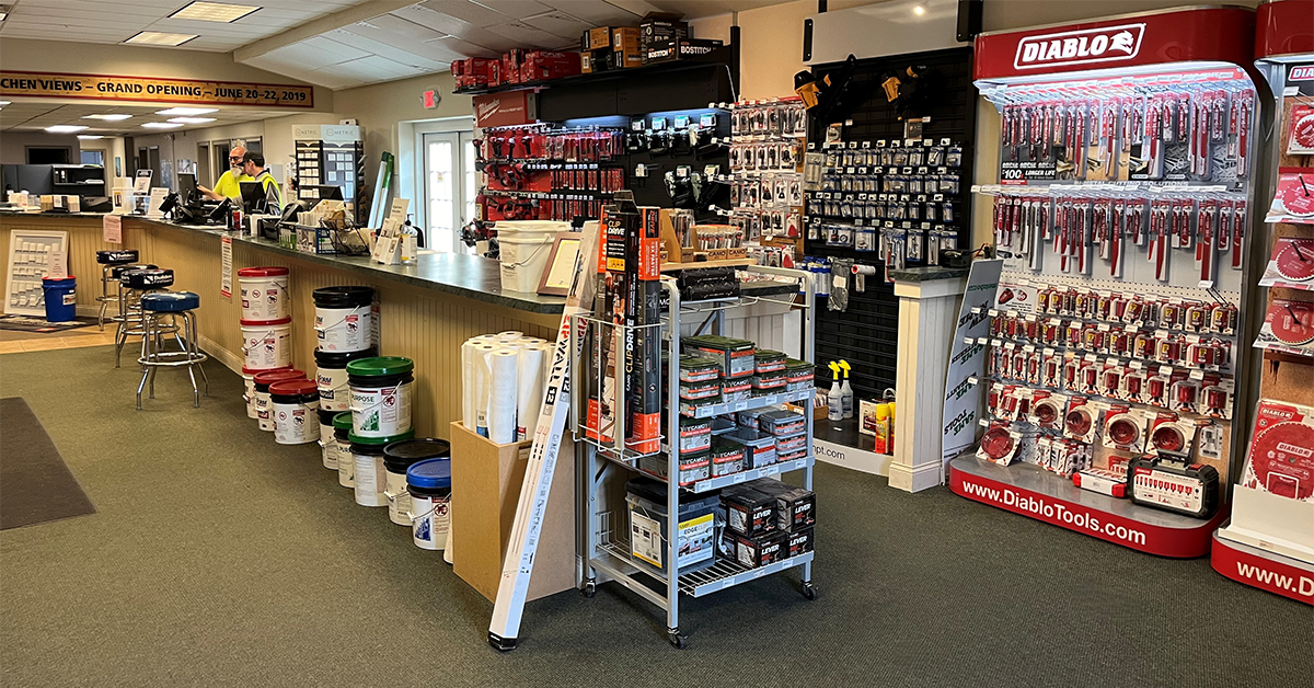 Interior of a showroom contractor service desk with buckets of materials, a countertop workspace, and walls stocked with hardware, tools, and accessories alongside a red Diablo tools display.