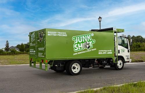 A side and rear perspective of the green Junk Shot junk removal truck, showcasing company branding,  