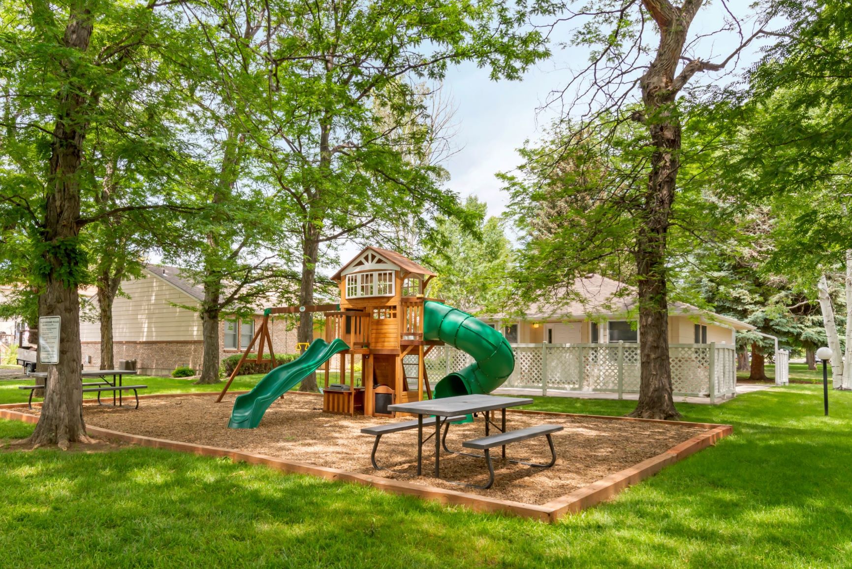 Community playground with two picnic tables, multiple slides, swings, and rock climbing wall.