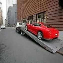 A red sports car sits securely on a flatbed tow truck in a downtown setting, demonstrating professional loading, safe transportation, dependable towing, and reliable vehicle recovery services with exceptional care.