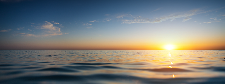 A calm body of water with the setting sun in the background.
