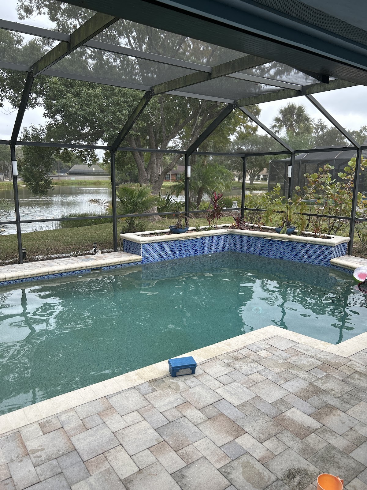 Screen-enclosed backyard swimming pool with a raised spa, stone paver decking, and a waterfront residential setting.
