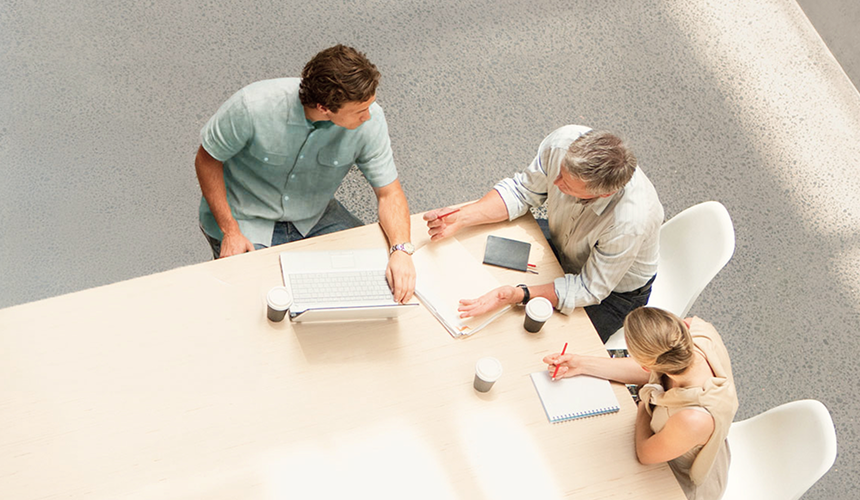 Three people working at a desk, as seen from above.