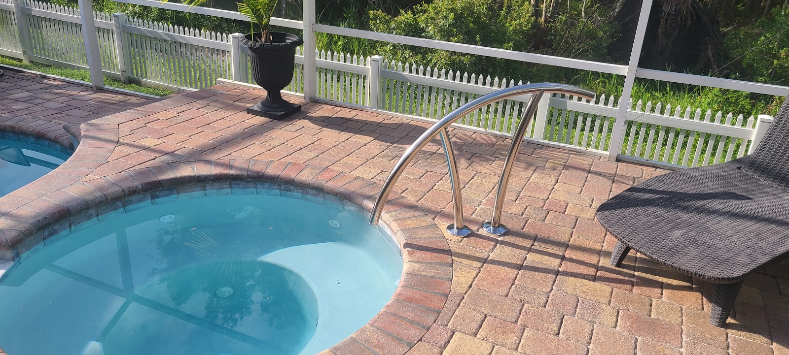 Backyard swimming pool and spa with curved edges, brick paver decking, stainless steel handrails, and a white railing.