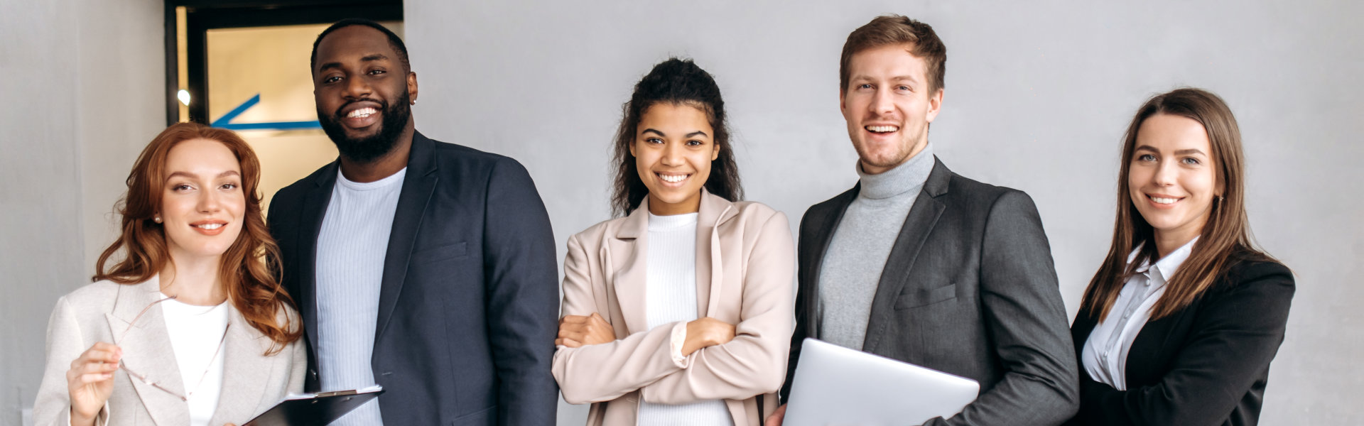 A diverse group of five professionals, three women and two men, stand side-by-side, smiling confiden 