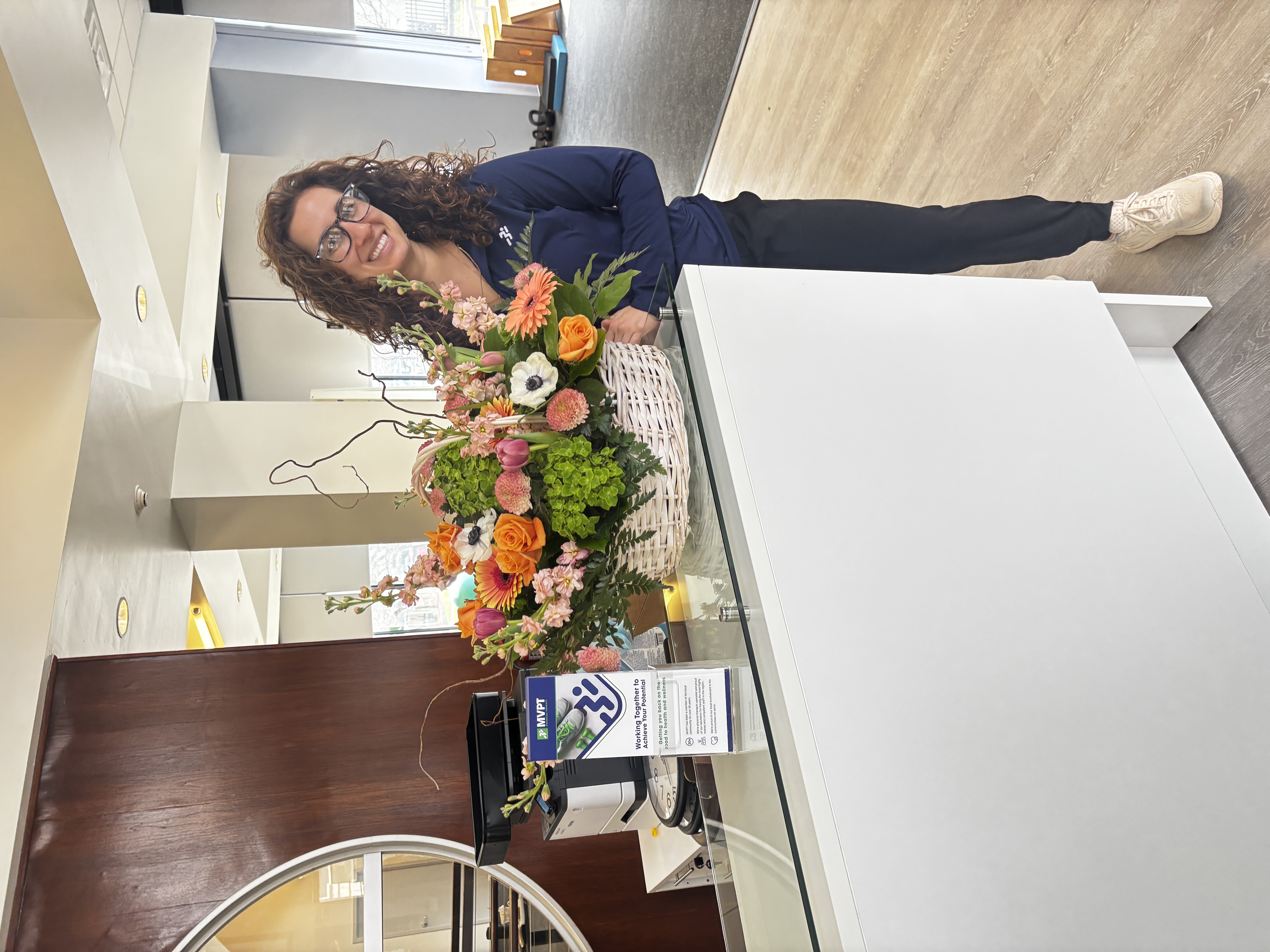 MVPT - Buffalo, NY Grand Opening 2026 Florianna PT, DPT at front desk area with flowers.
