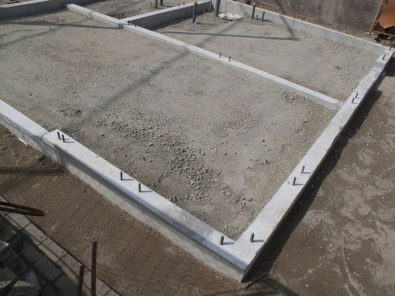 A newly poured concrete foundation slab shows the initial framework of a building's base, with reinforcing bars protruding, set on a gravel bed, ready for further construction.