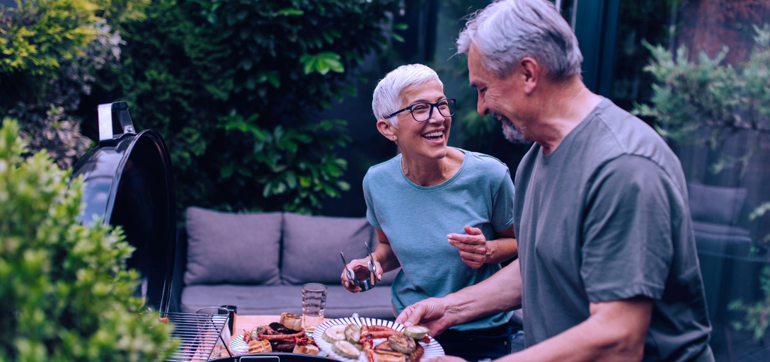 A retired couple barbecuing together outside.