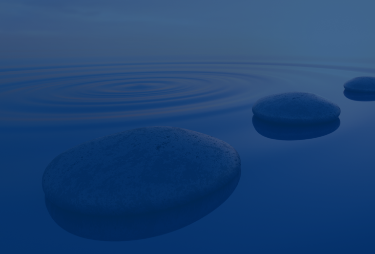 A path of smooth, round stones in a rippling lake under a pink and orange sky.