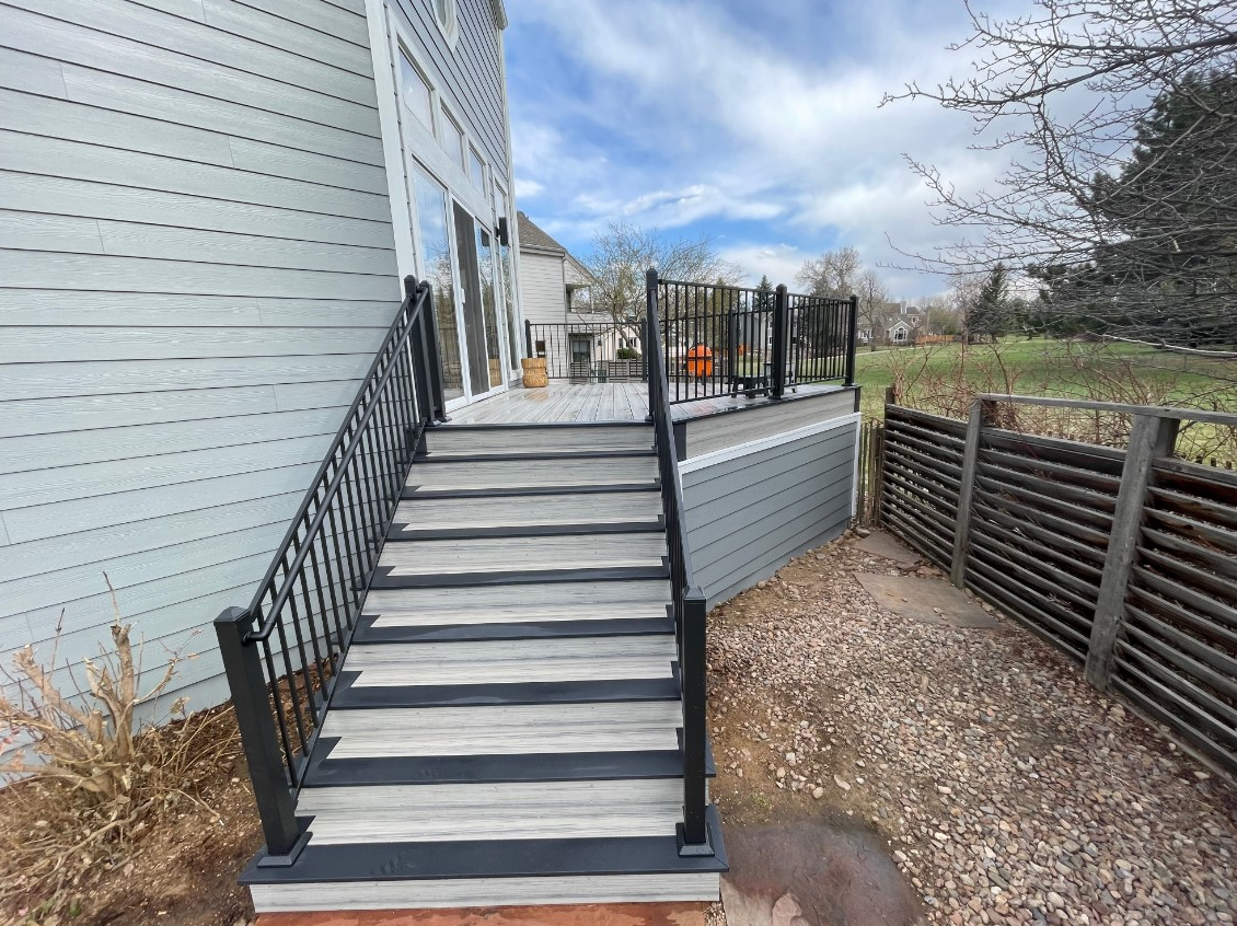 A triangle shaped composite deck with a staircase coming off the side of the deck. Deck has steel railings with ADA compliant handrail on stairs. The deck is enclosed around the underside of the deck with a wall of siding to keep animals out.