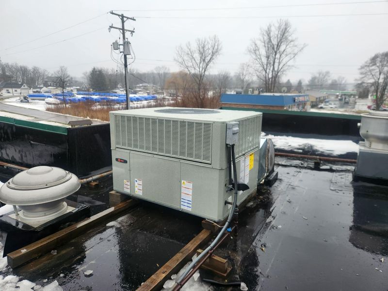 A large Trane rooftop unit (RTU) is installed on a flat commercial roof during winter. The high-efficiency HVAC system provides heating and cooling, featuring weather-resistant housing and electrical disconnects.