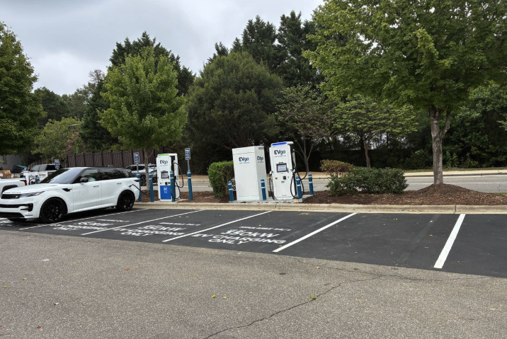Several EVgo fast charging units installed in marked parking spaces at a public charging station, with EVgo logos on the chargers, protective bollards around each unit.