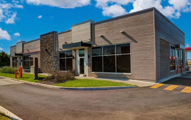 Modern commercial building exterior featuring large glass storefront windows, contemporary architectural elements, and landscaped surroundings. The property showcases professional commercial real estate development, retail business space, and modern construction design suitable for offices or service-based businesses.